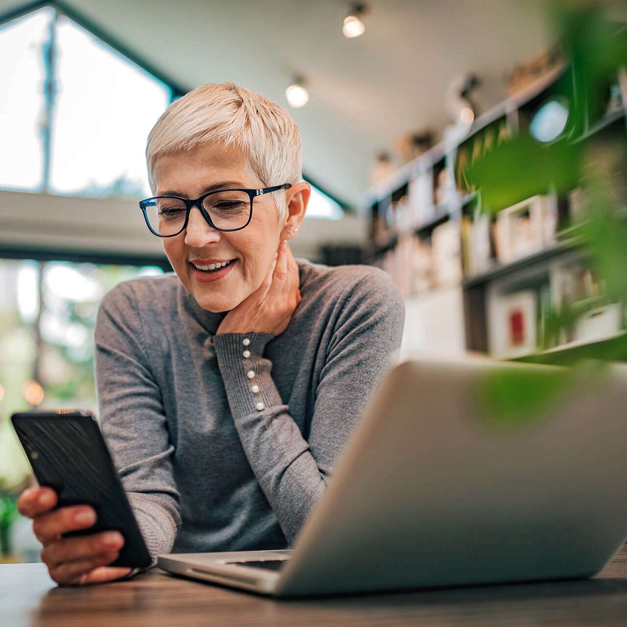 Woman using a phone sitting at a laptop