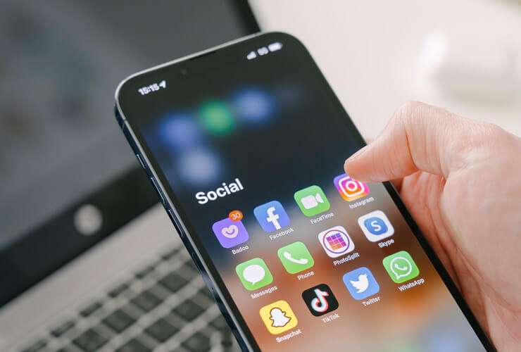 Hand selects social media icons on a mobile phone being aware of red flags that can help spot possible social media impersonation schemes such as unusual profile info, unsolicited messages, or suspicious posts.